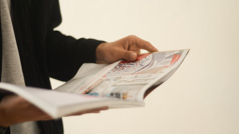 Een persoon houdt in zijn handen een tijdschrift opengeslagen vast. 