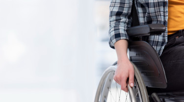 Zichtbaar is een arm en een deel van de romp van een persoon in een rolstoeldeel waarbij de hand rust op het wiel.