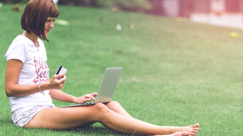 Vrouw zit op het gras en leest vanaf een laptop