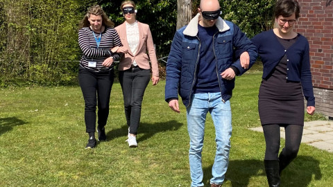 Deelnemers maken een wandeling met een blinddoek onder begeleiding