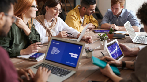 Een groep mensen zit aan tafel met laptops te overleggen.