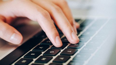 een toetsenbord met daarop een hand, waarbij de vingers op de toetsen rusten