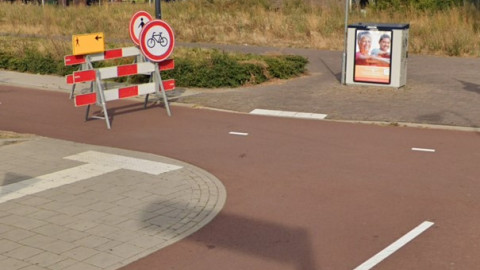 Een onveilige en onoverzichtelijke verkeerssituatie voor voetgangers met obstakels zoals een verkeersbord op het fietspad en een elektriciteitskast op de stoep aan het einde van de geleidelijnen.