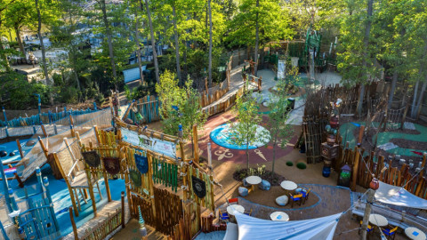 Een terras met stoelen en tafels omringd door groene bomen in een pretpark