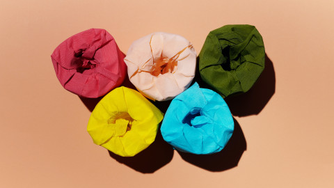 Vijf wc-rollen met gekleurd papier eromheen. Van bovenaf gefotografeerd tegen een zalmkleurige achtergrond.