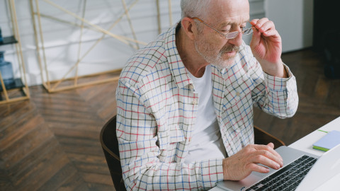 oudere man zit achter laptop en kijkt fronsend door zijn leesbril