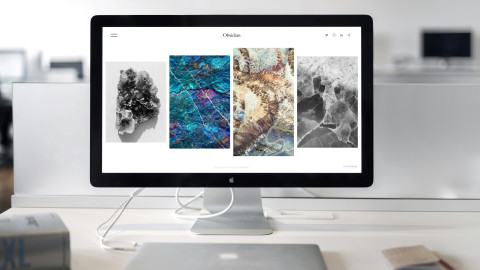 Op een tafel staat een computerscherm van Apple met daarop zichtbaar een websitepagina met vier natuurfoto's in verschillende kleuren.