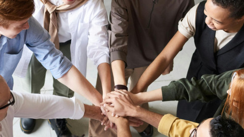 acht personen staan in een kring en hebben hun arm uitgestrekt en de handen op elkaar gelegd