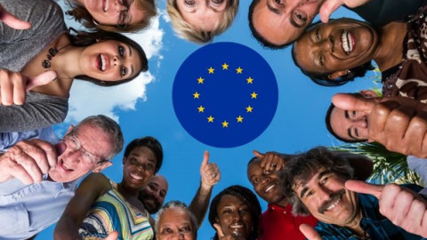 Een blauwe cirkel in het midden waarin een cirkel met gele sterren staan waarmee gerefereerd wordt aan de EU. De blauwe cirkel is geplakt op een lichtblauwe lucht met waarop ook een wolk te zien is en om de blauwe cirkel staat een groep mensen in een cirkel voorovergebogen met hun duim omhoog. Ze kijken als het ware naar beneden in de camera.