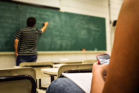 Man schrijft op groen schoolbord, leerling heeft smartphone