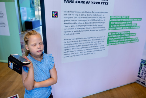 meisje luistert naar gesproken tekst bij bord in museum