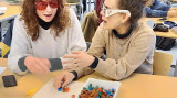 twee jonge vrouwen met bril spelen met lego aan een tafel