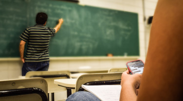 Man schrijft op groen schoolbord, leerling heeft smartphone