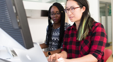 Twee vrouwen werken achter een desktopcomputer aan toegankelijke code