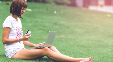 Vrouw zit op het gras en leest vanaf een laptop