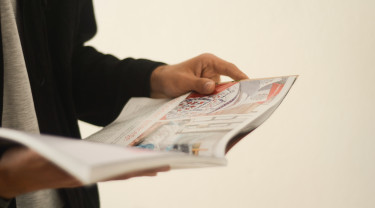 Een persoon houdt in zijn handen een tijdschrift opengeslagen vast.