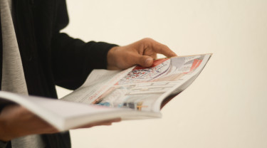 Een hand houdt een tijdschrift vast alsof deze persoon er doorheen bladert.