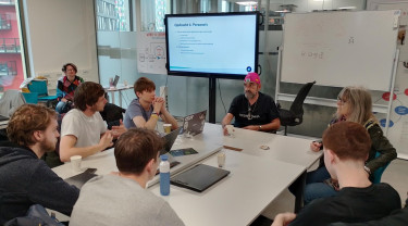 zes studenten zitten aan tafel en luisteren naar ervaringsdeskundige Vincent