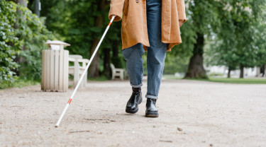 Een persoon loopt over een wandelpad in een park met geleidestok.