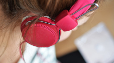 De zijkant van een hoofd van een vrouw, die een roze koptelefoon op heeft.