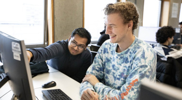 Twee jongens zitten achter een computer en lachen