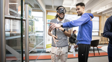 Twee studenten oefen met het lopen met een stok, een van hen draagt een blinddoek