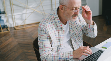 oudere man zit achter laptop en kijkt fronsend door zijn leesbril