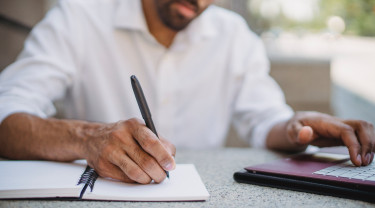 man met pen, schrijfblok en laptop