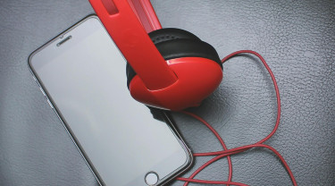 Een iphone ligt gekoppeld aan een rode koptelefoon op een zwarte tafel.