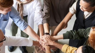 acht personen staan in een kring en hebben hun arm uitgestrekt en de handen op elkaar gelegd