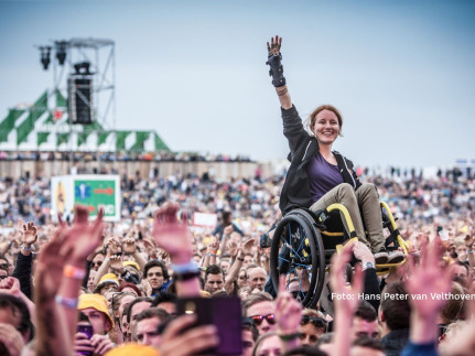 Een jonge vrouw crowdsurfing in rolstoel tijdens een optreden in de buitenlucht; foto Hans Peter van Velthoven