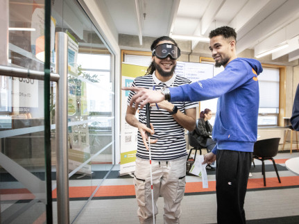 Twee studenten oefen met het lopen met een stok, een van hen draagt een blinddoek