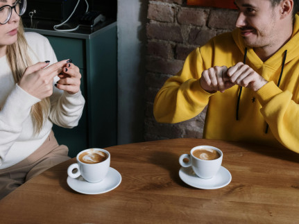 Twee mensen zitten aan tafel met een kopje koffie en praten met handgebaren