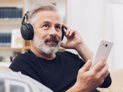 Een ervaringsdeskundige met koptelefoon en mobiele telefoon in zijn hand zit op de bank