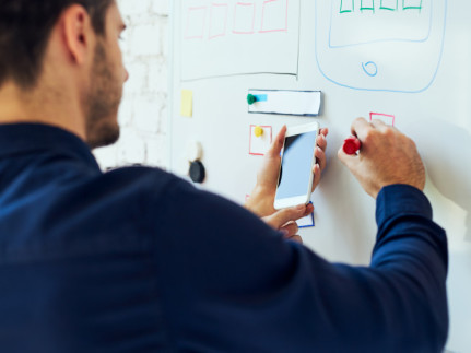 Een man schrijft op een whiteboard en houdt in zijn andere hand een mobiel vast die hij gebruikt als bron voor wat hij opschrijft - Wat is UX design