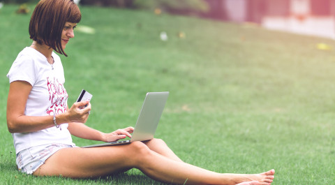 Vrouw zit op het gras en leest vanaf een laptop