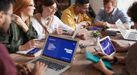 Een groep mensen zit aan tafel met laptops te overleggen.