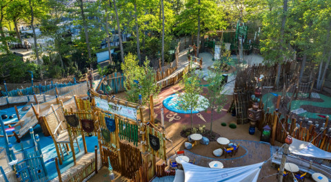 Een terras met stoelen en tafels omringd door groene bomen in een pretpark