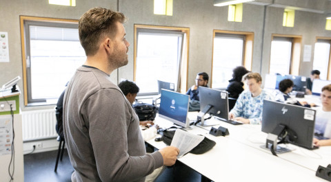 Docent staat voor de klas, jongens zitten achter computerscherm