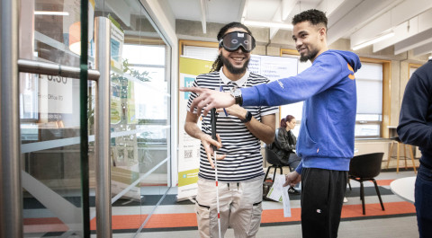 Twee studenten oefen met het lopen met een stok, een van hen draagt een blinddoek