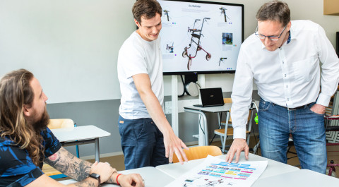Lector Eric Velleman buigt zich over een document op tafel samen met twee studenten