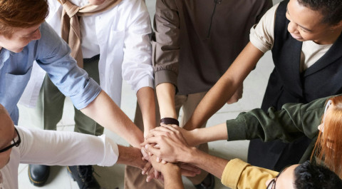 acht personen staan in een kring en hebben hun arm uitgestrekt en de handen op elkaar gelegd