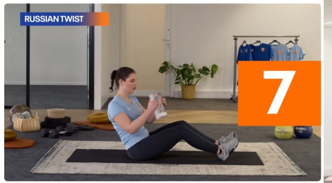 Een dame in zwarte broek en lichtblauw shirt en sportschoenen zit op de grond met haar knieen licht gebogen en een rechte rug. Ze houdt een boek in haar handen en doet de sportoefening russian twist.